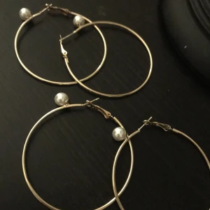 Två bar likadana guldiga örhängen  - Två par lika örhängen i färgen guld som är runda och har även vita pärlor uppe på örhängen 