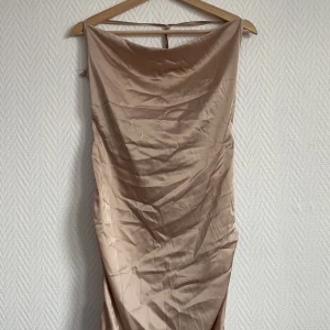 Beige klänning  - Beige nude klänning som är halterneck med öppenrygg  Snörning vid sidorna som man själv kan justera, samma med bandet runt nacken  Fick av en kompis men för stor för mig så andvändes ej 