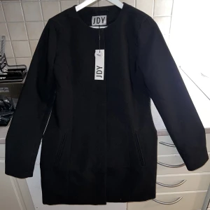 Stilren vårkappa - Oanvänd vårkappa storlek S. Köpt på zalando för 449kr, prislapp kvar. Går över rumpan och lite till. Dolda knappar. 