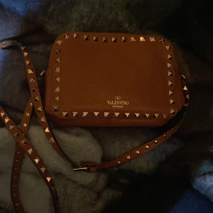 Valentino Rockstud Camera Bag - Säljer nu min super snygga valentino väska då den tyvärr aldrig kommer till användning. Endast använd enstaka gånger. Köpt på NK i Göteborg för  13 000kr, extra nitar tillkommer. Är i helt nytt skick.  Önskas fler bilder så skickar jag gärna det. 
