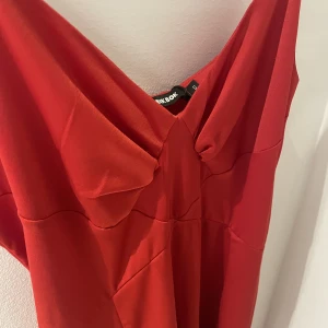 Balklänning - Vacker röd klänning, perfekt till en bal. Helt oanvänd. Spagettiärmar och går ner till fötterna. Sitter åt upptill och mer böljande nedtill. Dragkedja baktill. 