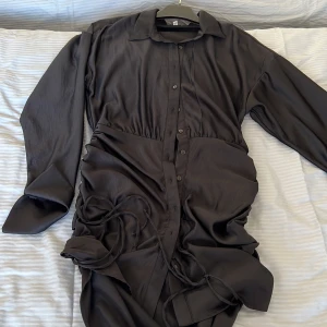 Nelly - Satinklänning där längden kan justeras genom att man drar i de snören som finns nertill. Använd en gång. 