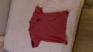 Polo Ralph LAUREN  - En rosa/röd t-shirt med ett lagom stort märke upp vid bröstet som är mörkblått, även ett märke på armdelen som är en 3a som även är mörkblått 