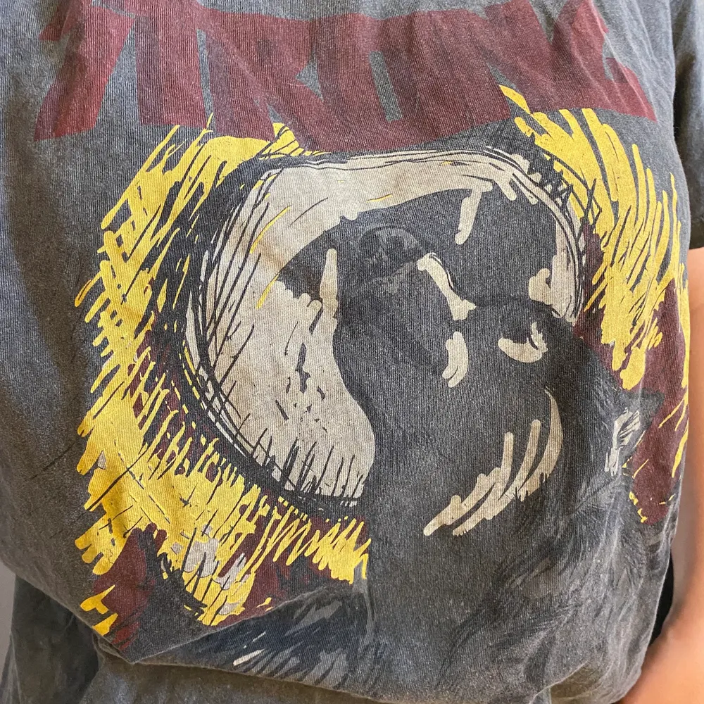 En grå tshirt med tryck från lager 157. På trycket är det en hund/ varg, en måne och texten ”strong” ovanför i rött.. T-shirts.