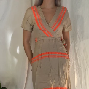 Mönstrad klänning - En söt beige klänning med mönster i neon-orange. Söt modell som slutar nedanför knäet.