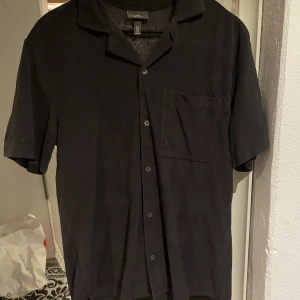 Frotté skjorta  - Mörkgrå kortärmad frotté skjorta från H&M med knappar hela vägen. Skjortan är i storlek M regular fit och använd 1 eller 2 gånger så i bra skick