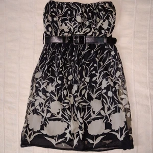 Svart/beige kort klänning med skärp/bälte - bandeau - Svart/beige kort klänning med ett svart avtagbart skärp. Resår upptill och under brösten där skärpet sitter, och med ett helsvart undertyg. Det mönstrade tyget är tunt och faller fint. Finns några dragna trådar men i övrigt är klänningen i fint skick. Storlek 8 som väl motsvarar XS/S.