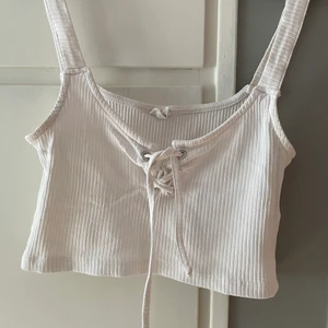 Linne med knytdetaljer - Ett vitt cropat ribbat linne med knyt detaljer super snygg nu till sommaren. köpt för några år sedan men använder bara inte längre, leverans går att lösa (köparen står då för frakten)