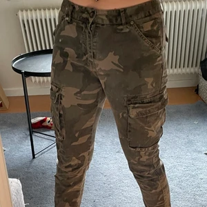 militärbyxor - ett par militärbyxor med två stora fickor på varsina sidor som går att öppna och använda, baksidan har två fickor som också går att öppna och använda. Byxorna är lågmidjade, byxorna är straight men sitter ganska så tajt.