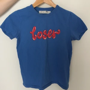 T-shirt Från Junkyard - Blå T-shirt med röd text från Junkyard. Slim fit. Köparen står för frakten.