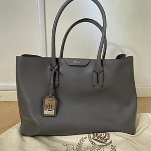 Ralph Lauren läder tote - Grått läder. Lauren Ralph Lauren. Dustbag medföljer. Fint skick men finns ett litet vitt märke fram (se bild) går eventuellt att gnugga bort. Rymmer både A4 och dator så fungerar fint som skol/arbetsväska. Nypris ca 3500kr.
