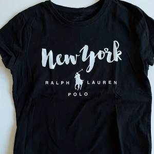 Ralph Lauren - Svart T-shirt med vitt tryck från Ralph Lauren i storlek XS. Pris 100 kr eller högstbjudande. Fint skick.