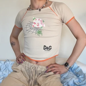 Vintage Dolce & Gabbana baby graphic tee - Sjukaste vintage Dolce & Gabbana beigea graphic baby tee med orangea detaljer längst ner, vid ärmarna och vid axlarna 🌺🦎 trycket på denna tröjan är stört snyggt och jag älskar även ringningen längst ner! Sitter perfekt och är så snygg till ett par vanliga jeans och ett par feta solglasögon nu till sommaren! 