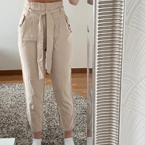 Beiga kostymbyxor - Beiga kostymbyxor från H&M med bälte! Byxorna sitter skönt och är mjuka. Använts fåtal gånger. Ingen retur. Alla plagg som säljs tvättas noga innan leverans! Det är bara att skriva om du har några frågor eller vill se fler bilder på plagget! <3