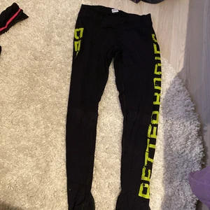 Träningstights från betterbodies - Lågmidjade träningstights från betterbodies med neongula text på sidan av benen. De har även en dragkedja vid vaden. Gott skick. 