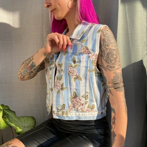 Jeansväst med blommor  - • Unik och cool väst • I jättebra skick och material. Randig i vita och ljusblå stripar, med rosor över. Två fickor på bröstet.