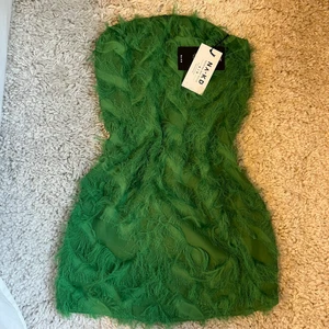 Grön tubklänning med faux fjädrar - Säljer denna gröna tubklänning med faux fjädrar från NA-KD. Aldrig använd och lapparna sitter kvar. Säljer då jag inte tycker att den passar mig. Kan mötas i sthlm eller Västerås. Vid frakt tillkommer fraktkostnad😊💕