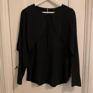 Cos blus silke - Svart blus i 100% silke från COS. Ärmarna ligger som ”vingar” ovanpå axlarna och faller ner till handlederna där man sticker genom handen för att hålla ärmarna på plats. Luftigt och tunt siden med vackert fall. Aldrig använd. Flexibel, passar S-L.