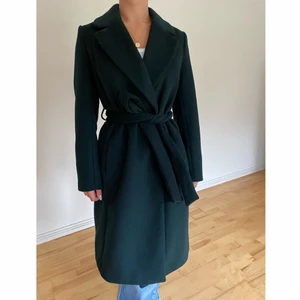 Mörkgrön kappa, storlek 34/36 - Mörkgrön och fodrad kappa från H&M. På mig (160cm) är den vadlång, lång i ärmarna & lite stor över axlarna. Strl: 34 men upplevs mycket rymlig, med plats för tjockare tröjor samt passar även storlek 36/S. Stängs med knytband samt dolda knappar. I nyskick!