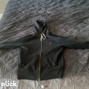 En Svart Ralph Lauren Hoodie - En fin hoodie från Ralph Lauren perfekt nu till kallare väder. Ett litet hål vid vänster armbåge finns men syns inte mkt och pga det de lägre priset. 
