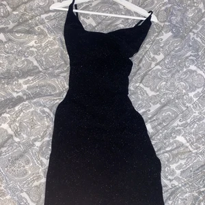 Klänning  - En jättefin svart tjat klänning, endast använd 1 gång. Materialet är lite glittrigt och den är stretchig, kryss i ryggen. 