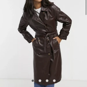 Trenchcoat  - Vinröd/brun kappa i läder. Strl S. Helt oanvänd. Den går under knäna strax på mig som är 1.68lång. Den är helt slutsåld på Asos hemsida!
