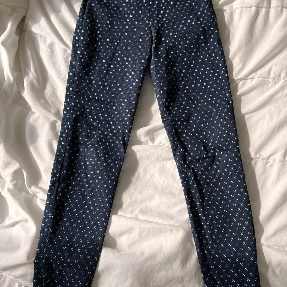 Mörkblå, kostymliknande byxor med vita detaljer på. Strl 32. Ankellängd. Sparsamt använda. Säljes pga för små. . Jeans & Byxor.