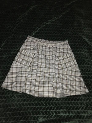 Kjol - Grårutig A-linjekjol med midjeresår och fickor. Barnstorlek 146-152 men passade mig som är 170cm lång, ca 94 cm runt höften och ca 63 runt midjan