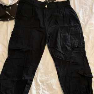 Cargobyxor - Svarta cargobyxor i storlek 1XL. Använda men inte slitna. Jättesnyggt att matcha med nån kedja på höften. Säljer då de inte används längre. Frakt tillkommer.