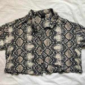 Ormskinnsmönstrad topp från Urban outfitters - Snygg topp i ormskinnsmönster, med liten krage och korta ärmar. Den är relativt kort. 
