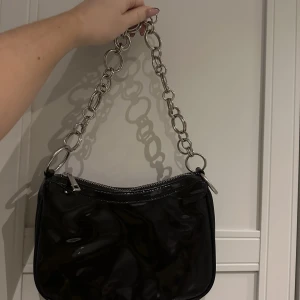 Väska - Säljer en svart lackad handväska från Nelly i nästan nyskick. 50:- köparen står även för frakt!