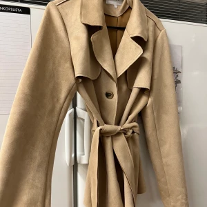 Kappa i mocka  - En kortare beige kappa i mocka från Vila.  Knappar & knytning runt midjan  Helt ny och oanvänd, i super fint skick! Storlek L. 