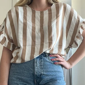 Randig blus  - Vit och brun randig blus från river island i storlek S. Knappen bak i nacken har en ögla som är trasig, går lätt att laga men själv har jag varit för lat och tagit en säkerhetsnål… Superskönt tunt material 