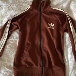 Brun adidas tröja - Brun adidas zip-up köpt på secondhand. Hittar inte strl men skulle säga att det är en M