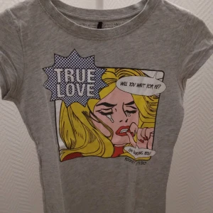 Grå topp/tee med Pop Art tryck, 'True Love'. Strlk: XS/34. - Grå topp/tee med Pop Art tryck, 'True Love'. Använd men i ok skick, inget trasigt etc. Se bilder för egen bedömning. Material: Bomull Storlek: XS/34.