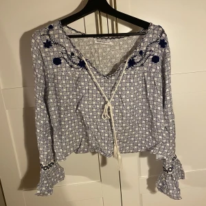 Blus - Blå mönstrad blus från Galmorous (tall) med v-ringning, snör/toffsdetalj, blå pärlor broderade i blommor, volanger i ärmarna. Nypris 399kr. Frakt tillkommer!!!!