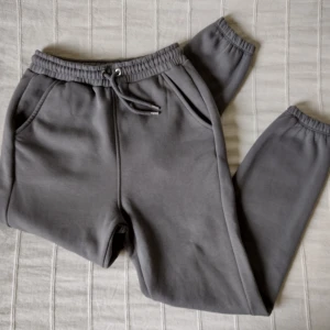 Grå högmidjade mjukisbyxor/joggers från Junkyard, storlek XS - Högmidjade mjukisbyxor från Junkyard i en skitsnygg grå färg. Väldigt mjuka och sköna. Använda endast ett par gånger. 65% bomull och 35% polyester. Storlek XS.