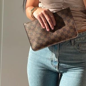 Louis Vuitton Neverfull pochette damier ebene - Säljer min Louis Vuitton Neverfull pochette damier ebene, den är i nyskick. Mått: 25 cm på längden och 15 cm på höjden. Kvitto medföljer.