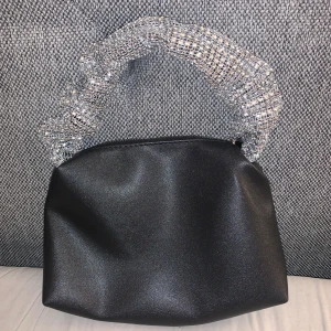 Svart glitter väska - Svart rymlig väska med silver glittrigt band. Köpte den endast för nyår och kommer inte använda mer. Väldigt fin och festlig. 