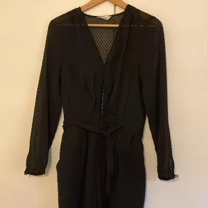Svart byxdress - Svar, lång byxdress med skärp i midjan och fickor. Frakt tillkommer 