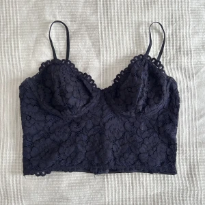 Söt croptop - Mörkblå croptopp i med spetsdetaljer. Rätt små kupor, dragkedja i ryggen (se bild 2). Gulddetaljer, strl 40 men passar även S. Oanvänd perfekt skick