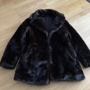 Mörkbrun varm pälsjacka. Faux fur. Har stora fickor och kan stängas med knappar. Har ett silkesliknande material på insidan.