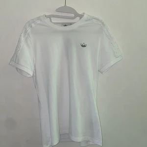 Adidas, T-shirt, Stl 40/MEDIUM - Nyskick - lappen sitter kvar. Köpt på Nelly i November 2021 för nypris 400 kr. T-shirten har väldigt fina glittrande paljetter på axlarna. 