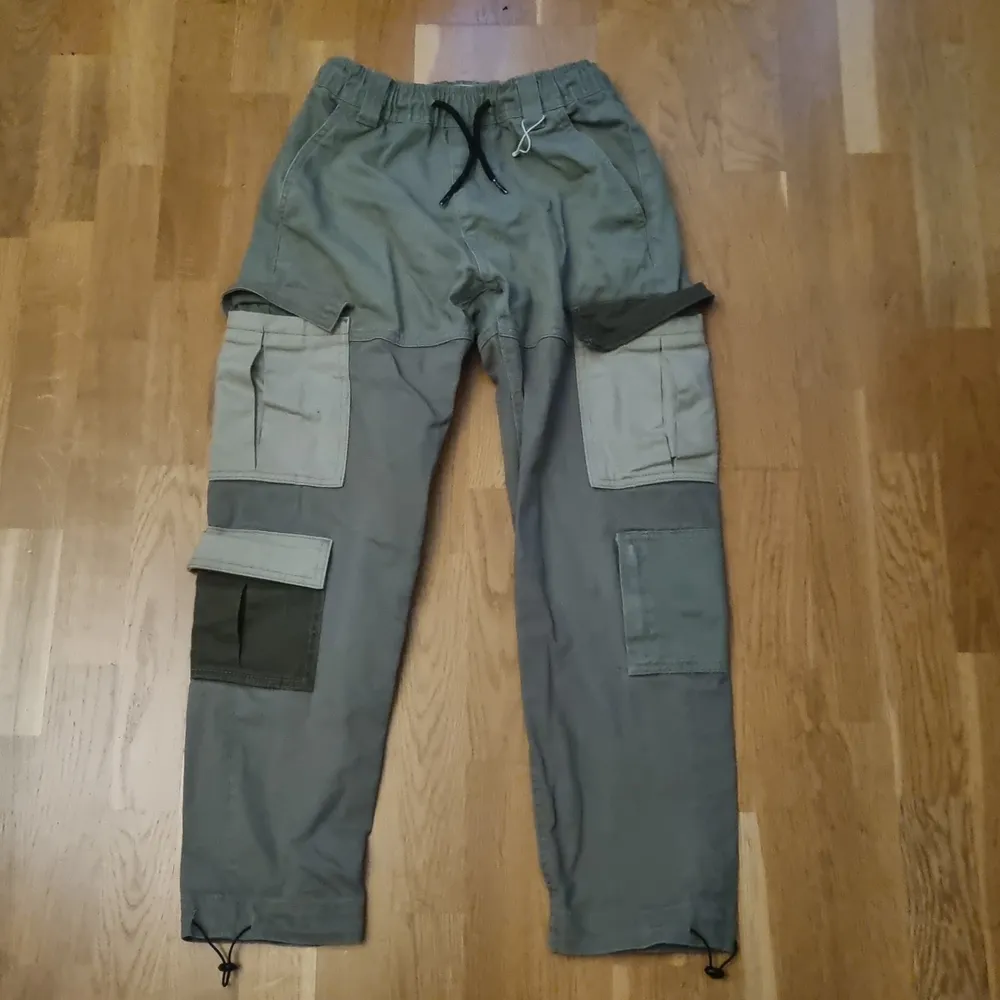 Gröna Cargobyxor med fickor av olika färger. Midja: 73 cm (flexibel), Längd: 90 cm. Jeans & Byxor.