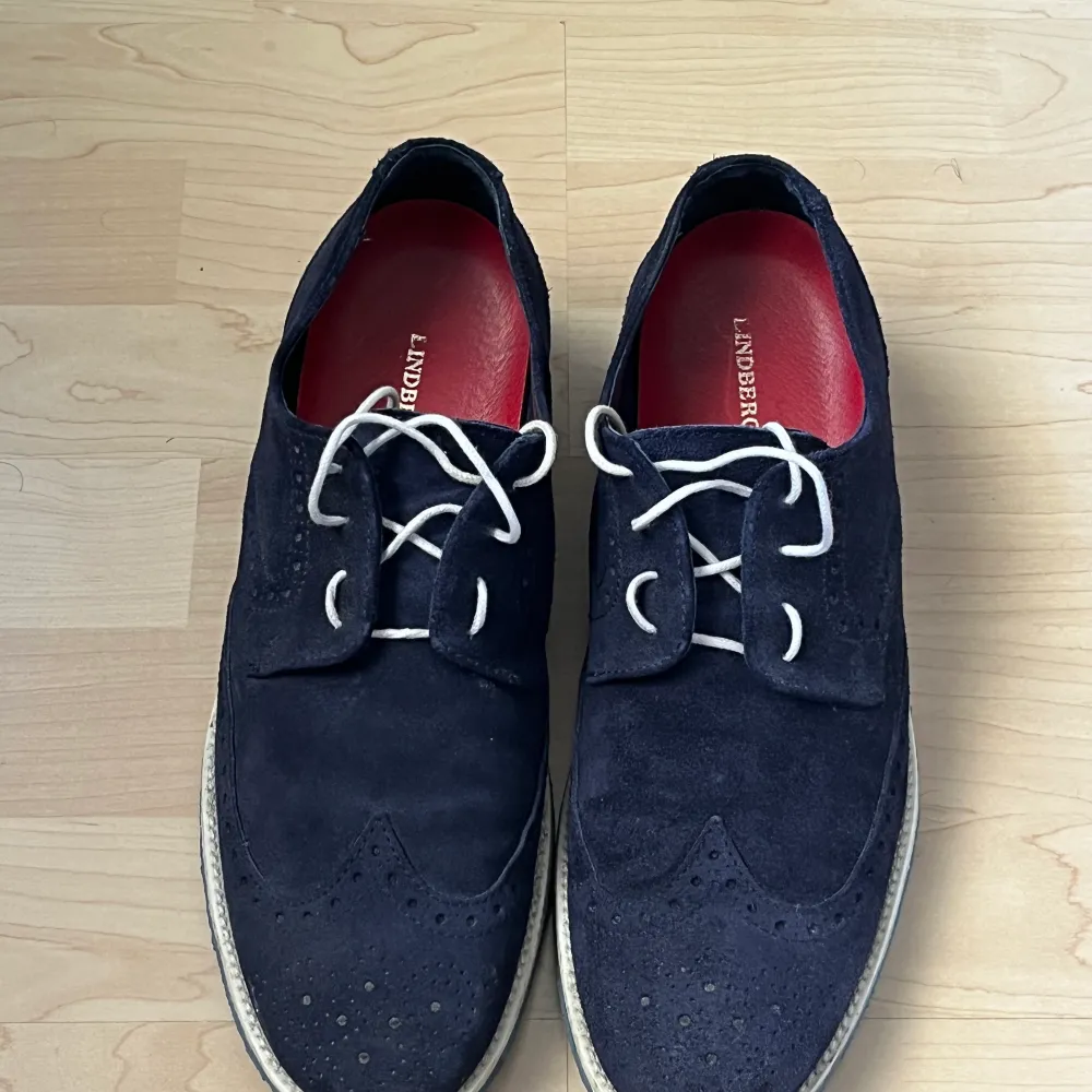 Ett par Lindbergh finskor. Färgen på skorna är mörkblå och underdelen av skorna är en lite ljusare nyans av blå. Storleken på skorna är 44. Skornas naturliga snöre är vit men det tillkommer även ett par ljusblå skosnören.  Köpt för 1499.  Säljs för 499. . Skor.