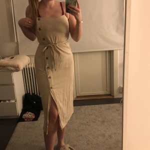 Beige klänning  - Säljer denna ”mörk beiga” klänningen då jag aldrig använt den och den är lite tajt i bysten, super skön med knappar på sidorna så de blir som en slitt nertill bandet runt magen får att ta lös
