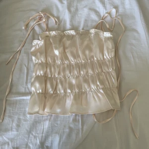 Topp - Oanvänd beige topp i glansigt material.