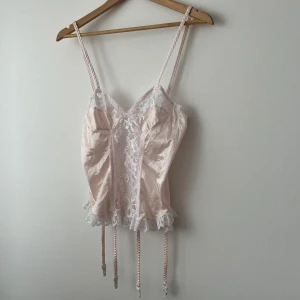 Rosa drömmig korsett-ig topp - Supersöt vintage korsett-ig topp med strumpebandshållare! 💌 Spets & satin. Storlek M enligt lapp, men passar säkerligen en XS-S.  Fint skick, har dock blivit missfärgad av föregående ägare på högra sidan och lite bakåt! Ganska långa axelband, kan knytas!