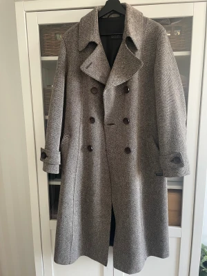 Lång kappa   - Beige-brun lång kappa i kanonskick. Material 65% ull, 25% polyamid och 10% silke. Ca 115 cm lång. Går ned till vaden på mig som är 178 cm. Mjuk och stilsam med skärp i midjan och ordentliga knappar. Köparen står för frakt. Hojta för fler bilder. ✅