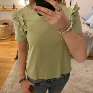 T-shirt med volanger - Sparsamt använd och jättefin ljusgrön t-shirt med volanger. Den är från zara och i 100% bomull. T-shirten är i storlek M men sitter bra på mig som brukar ha S så skulle säga att den passar st 34-38.